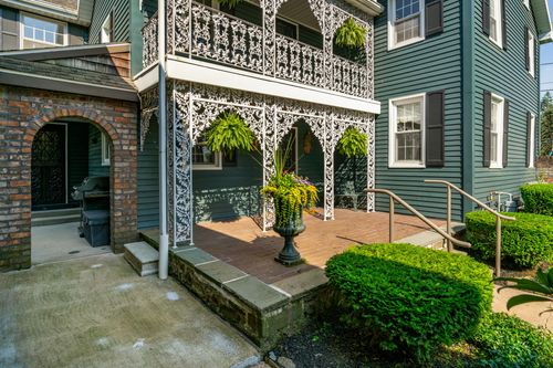 Brick-paved courtyard beneath an ornate ironwork balcony with potted ferns and a stone archway