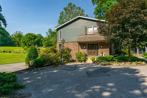 Brick and gray-sided home with a wood door entry and mature landscaping along the driveway
