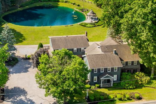 Aerial close-up of a blue-gray farmhouse with wraparound porches and dormer windows