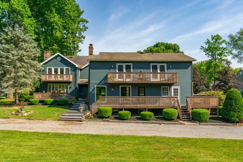 Rear exterior of a large blue-gray home with multiple wood decks and a stone chimney
