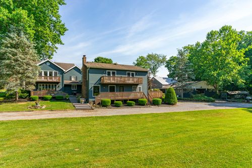 Blue-gray home with multi-level wood decks and balconies overlooking a wide lawn