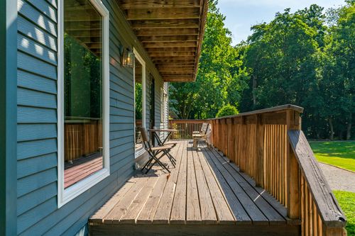Covered wood deck with cafe table and chairs running along the side of a gray home