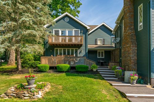 Blue-gray home with a wood balcony, deck and stone-edged flower bed in the backyard