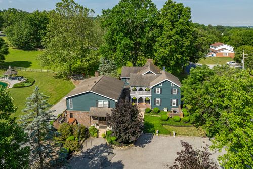 Aerial view of a two-story farmhouse with covered porches and manicured landscaping