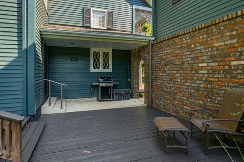 Covered wood deck with a gas grill and lounge chairs beside a brick exterior wall