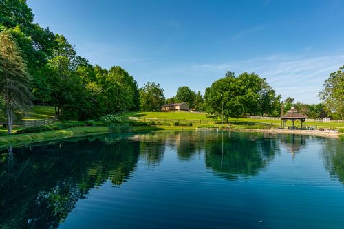 Emerald pond reflecting surrounding trees with a gazebo and open lawn beyond