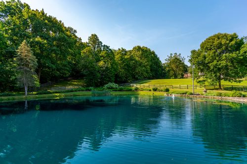 Tranquil pond bordered by a split-rail fence, mature trees and rolling lawn