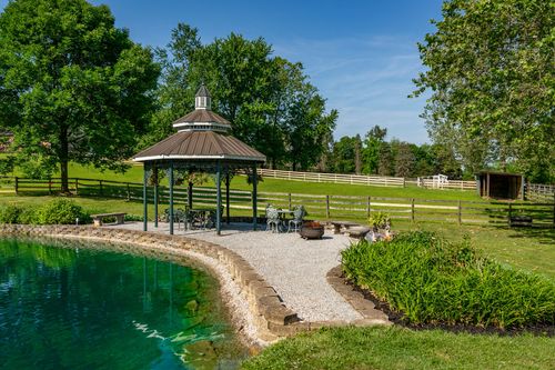 Lakeside gazebo with a gravel patio and seating overlooking a green pond