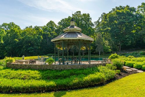 Wood gazebo with hanging flower baskets beside a pond and stacked-stone retaining wall