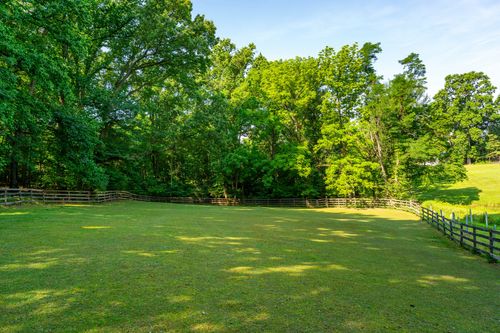 Split-rail fenced pasture with a mown grass clearing framed by woodland