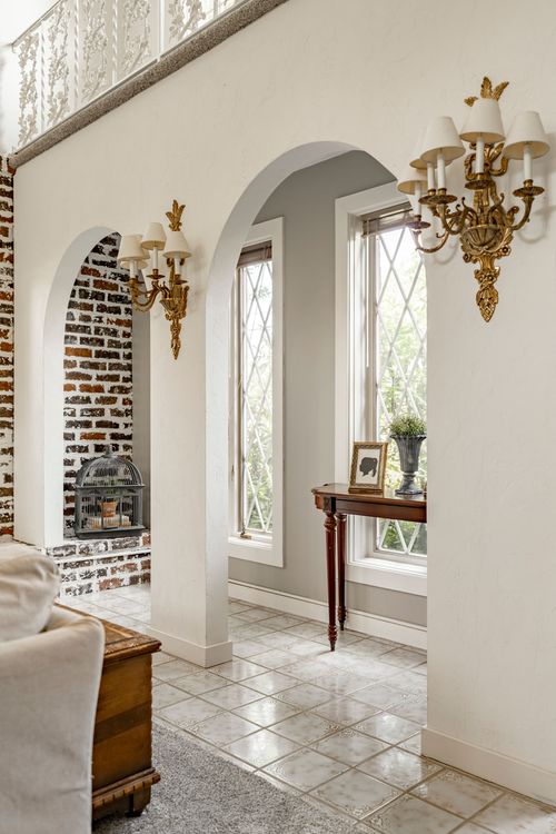 Arched doorway framing a brick fireplace nook with brass sconces and a console table