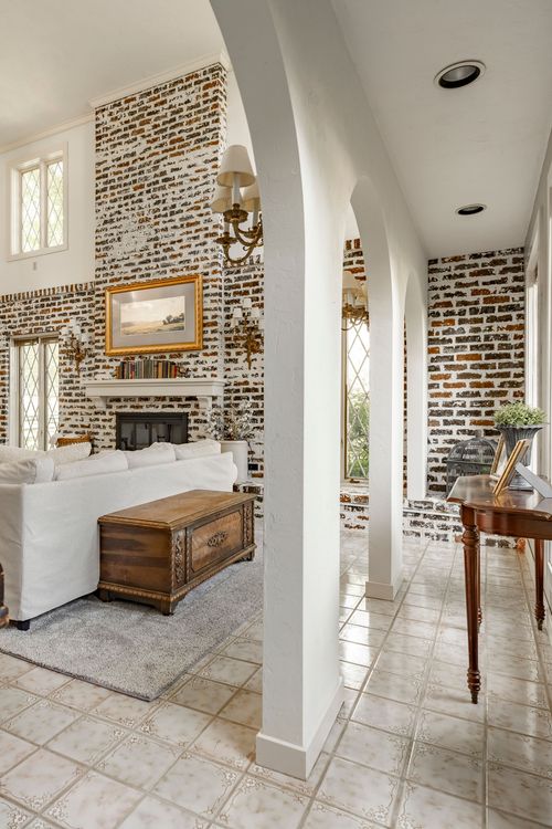 Living room with brick fireplace opening to a tiled hallway through arched columns