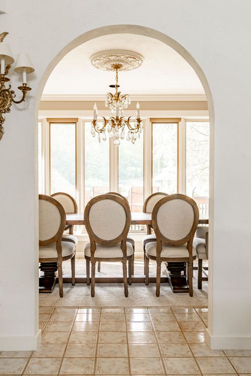 Dining room framed by an archway, with round-back chairs and a crystal chandelier