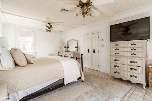 Bedroom with an iron bed, wall-mounted TV over a dresser and dual ceiling fans