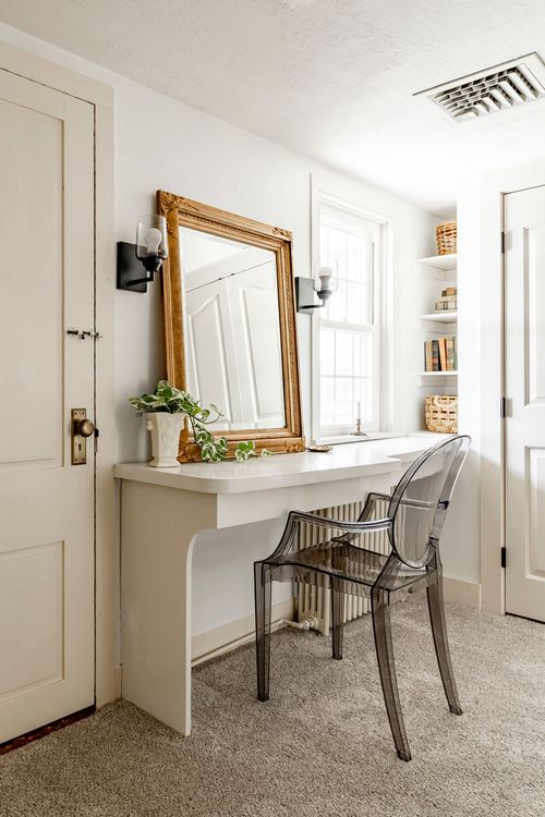 Small home office with a gilt mirror, white desk and clear acrylic chair