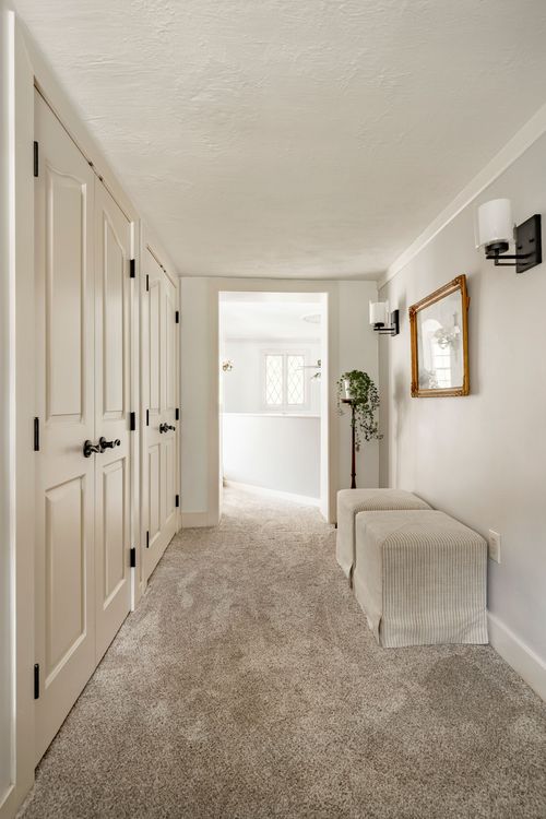 Hallway with white paneled closet doors, a gilt mirror and upholstered bench