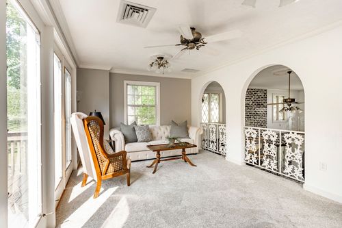 Sitting room with a tufted sofa and cane wing chair beside an arched stair landing