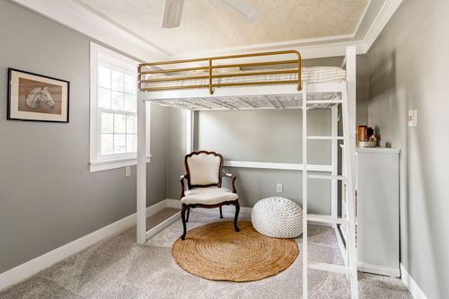 Kid's bedroom with a white loft bed over a desk and a round jute rug