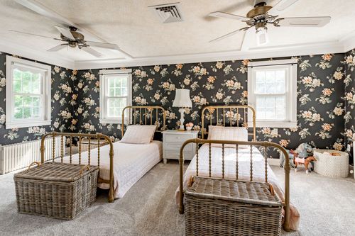 Twin bedroom with dark floral wallpaper, brass spindle beds and woven baskets