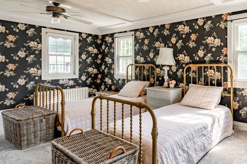 Twin bedroom with matching brass beds set against dark floral wallpaper