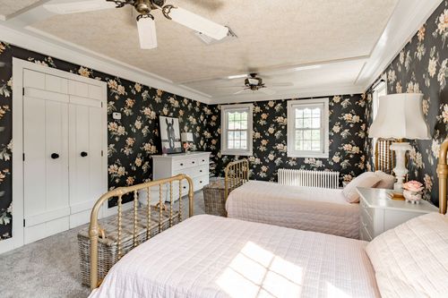 Bedroom with floral wallpaper, a brass spindle bed and woven storage baskets
