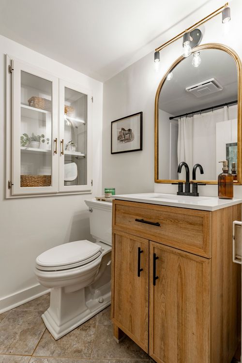 Bathroom with a repurposed wood vanity, arched gilt mirror and glass cabinet