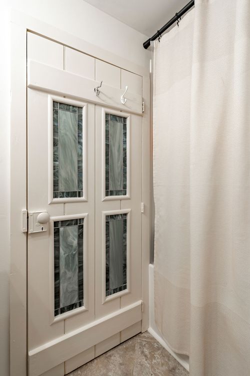 Bathroom detail of a stained-glass paneled door beside the shower curtain