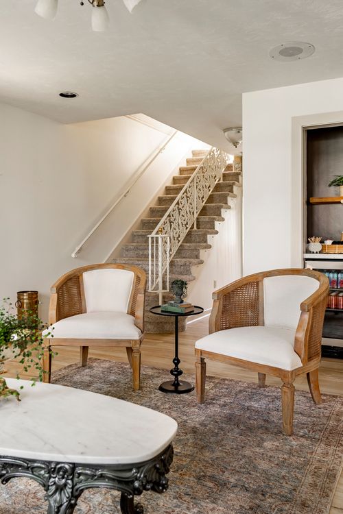 Sitting area with cane barrel chairs, a marble coffee table and carpeted staircase