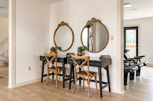 Entry nook with two round gilt mirrors above a black desk and wood chairs