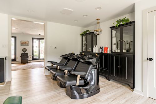 Hallway view into a salon shampoo area with black cabinetry and a pendant light