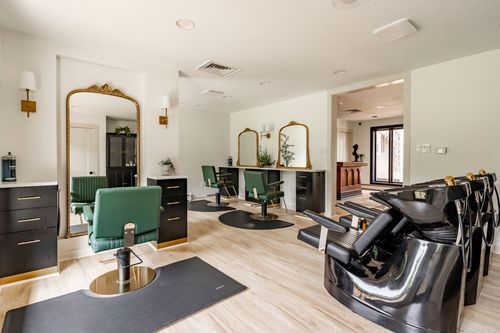 Wide salon view with styling chairs, gilt mirrors and shampoo bowls along light wood floors