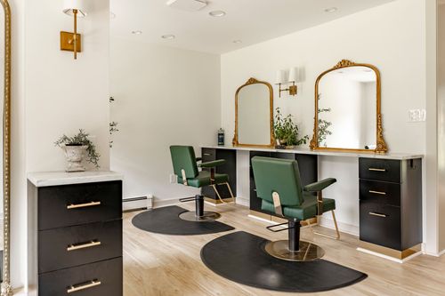 Twin salon styling stations with green chairs, arched gilt mirrors and black cabinetry