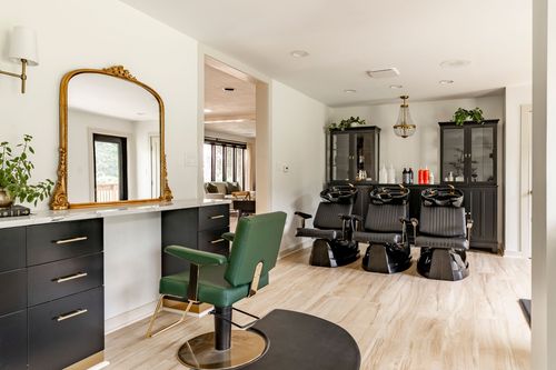 Salon styling station with an arched gilt mirror and green leather chair on light wood floors