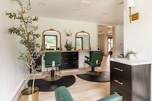 Salon styling stations with gilt mirrors, green chairs and a potted olive tree