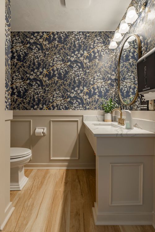 Powder room with navy chinoiserie wallpaper, marble vanity and a round brass mirror