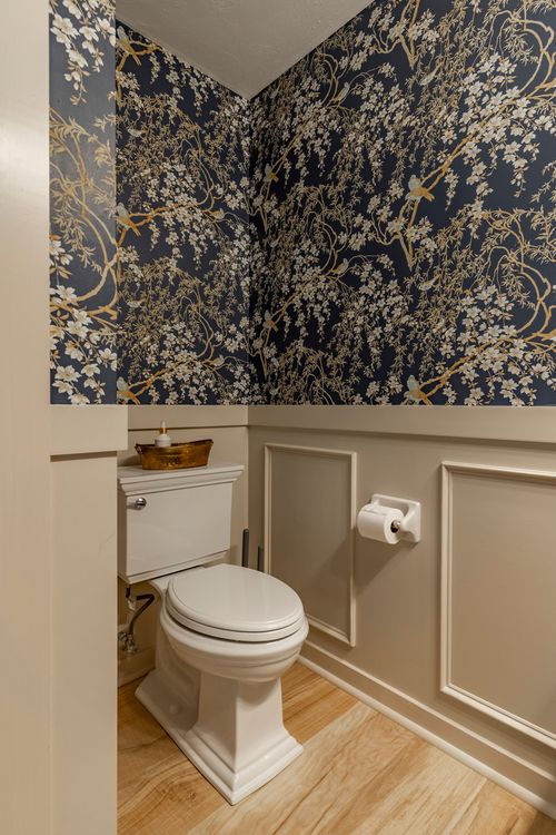 Powder room with navy bird and floral wallpaper above cream wainscoting