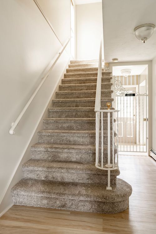 Close view of a carpeted staircase with a white wrought iron balustrade