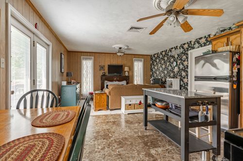 Kitchen and dining combo with wood paneled walls, floral wallpaper accent and a ceiling fan