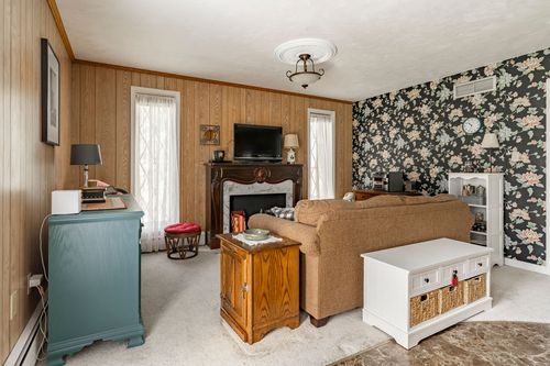 Living room with wood paneled walls, a floral wallpaper accent wall and brick fireplace