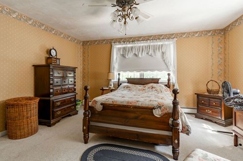 Bedroom with a four-poster wood bed, floral wallpaper border and a ceiling fan chandelier