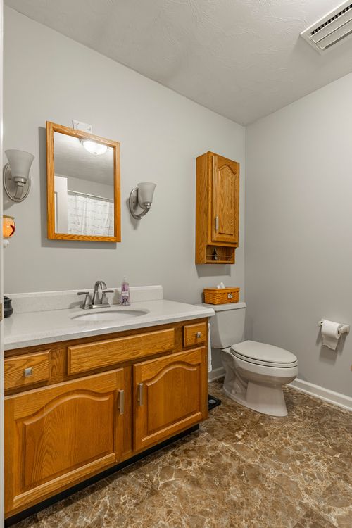Bathroom with an oak vanity, wall cabinet above the toilet and stone-look tile floor