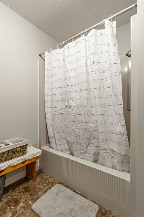 Bathtub with a patterned white shower curtain beside a wicker basket and wood bench