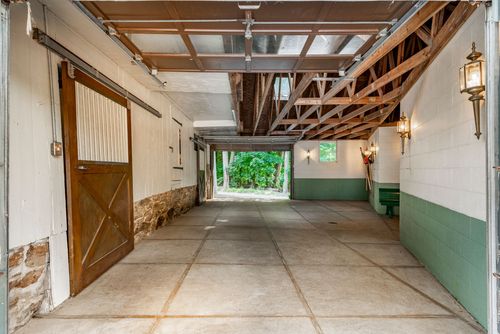 Barn aisle with a sliding wood stall door and stone accent opening to greenery beyond