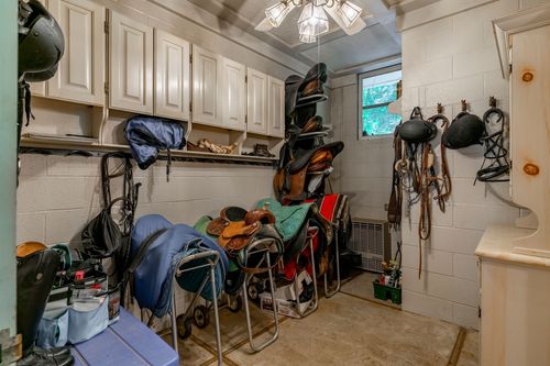 Tack room with saddle racks, hanging bridles and white cabinetry along a coffered ceiling