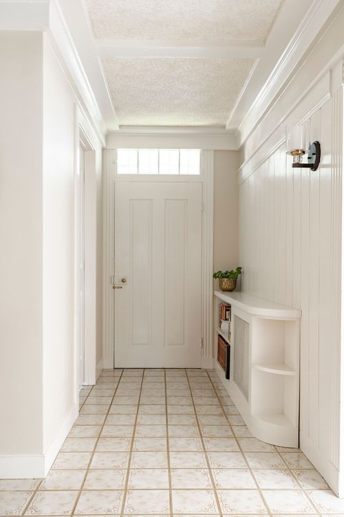 Neutral tile entry hallway with paneled wainscoting, a built-in corner shelf and glass-topped front door