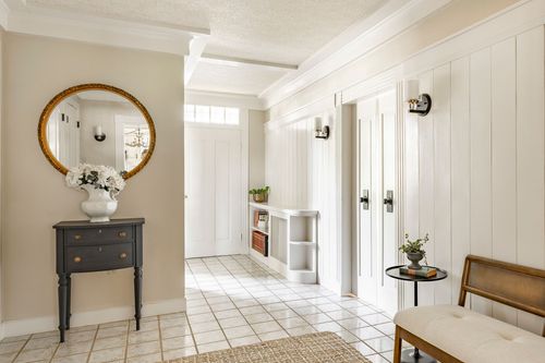 Foyer with a round gilt mirror over a dark console table, tile floor and wall sconces