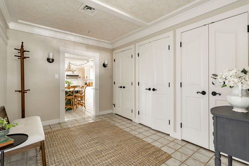 Mudroom hallway with white paneled closet doors, a coat rack, bench and tile flooring