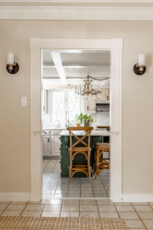 Arched doorway framing a farmhouse kitchen with green island, chandelier and cross-back stools