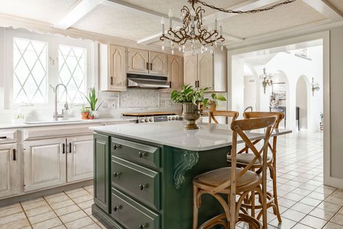 Kitchen with exposed wood beams, a brass chandelier, cream cabinets and a forest green island