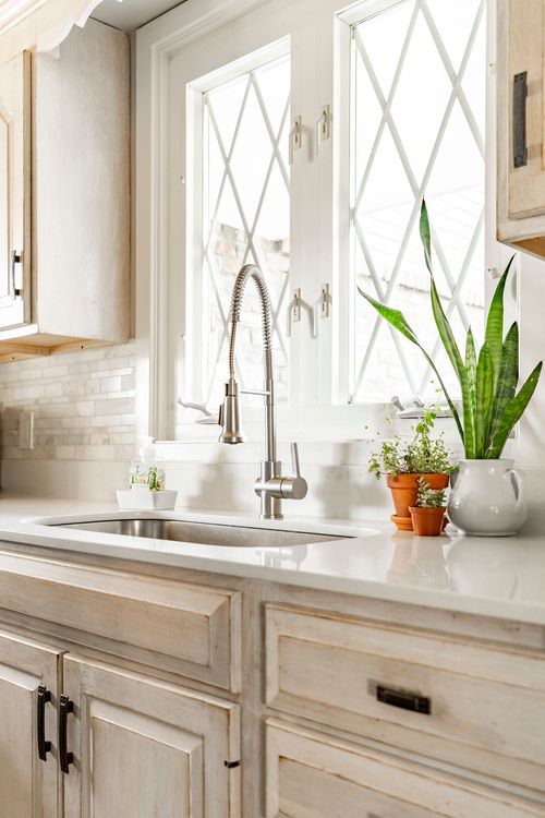 Close view of a kitchen sink with brushed nickel faucet, quartz counters and potted herbs